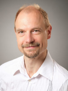 A man with a beard, blond hair and a white shirt.