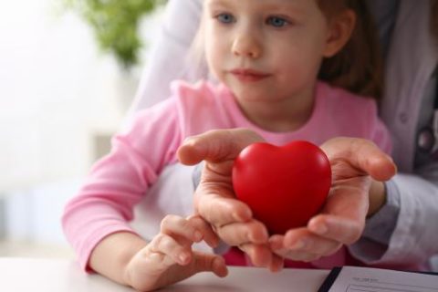 Little baby girl visiting doctor holding in hands red toy heart