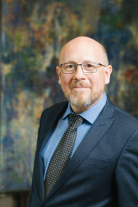 Ein Mann mit Brille in Anzug und dunkler Krawatte.