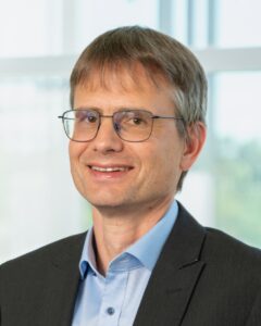 A man wearing glasses, a suit and a blue shirt.