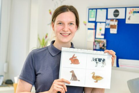 Eine Frau in blauem Shirt hält eine Bildtafel mit vier Tieren hoch.