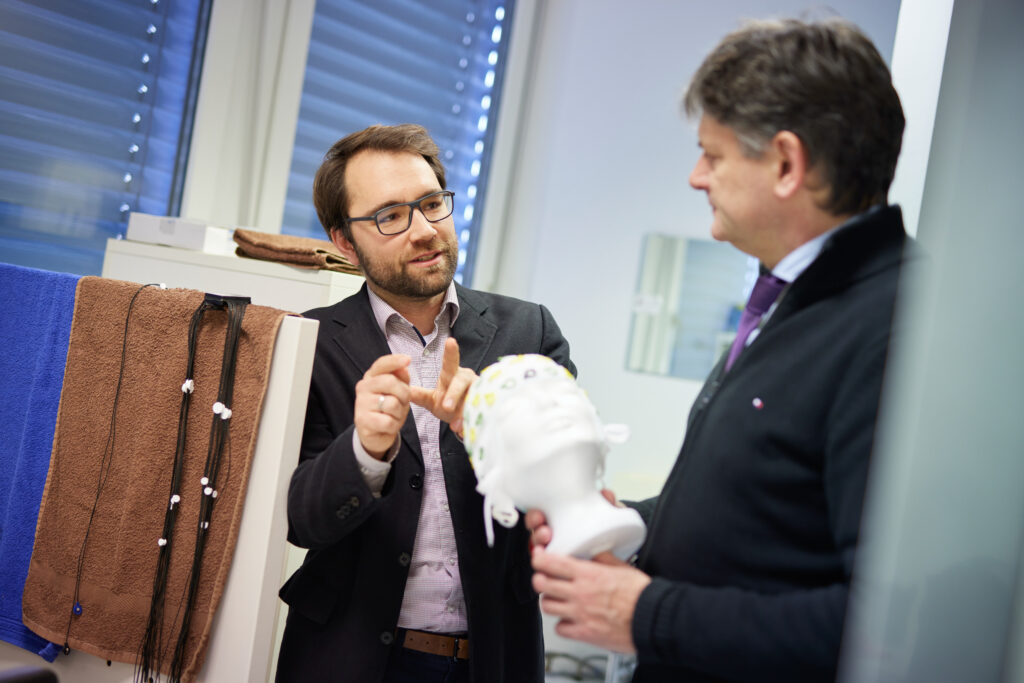 Zwei Männer im Gespräch. Einer der Männer erklärt dem anderen etwas. Der andere Mann hält ein Kopf-Modell in der Hand.