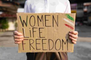 Eine Frau hält ein Schild in den Händen. Darauf steht "Women Life Freedom".