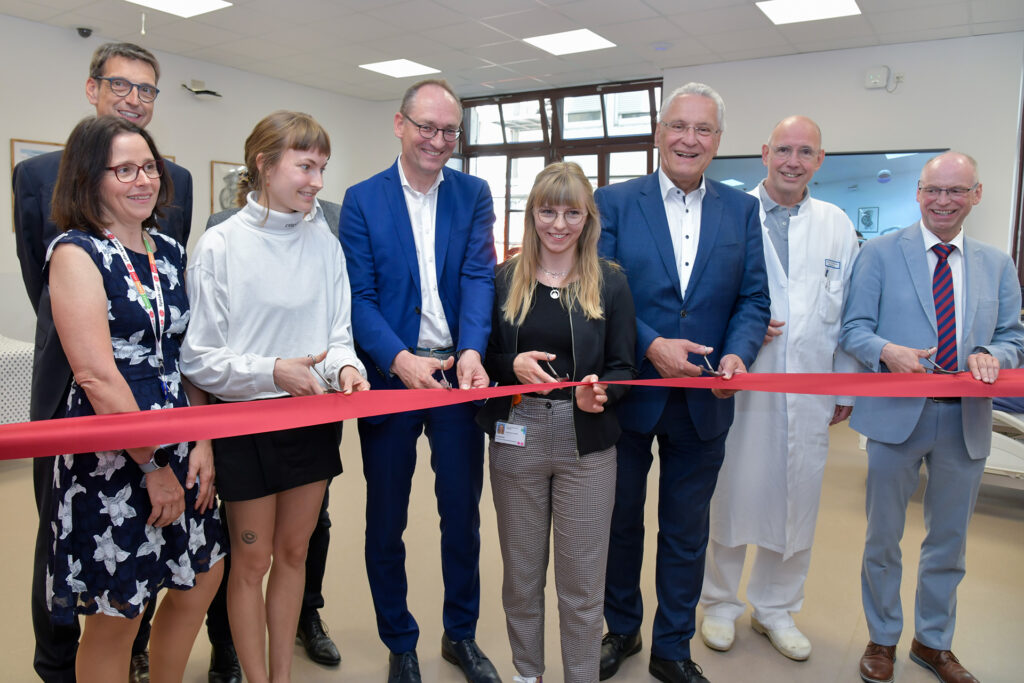 Gruppenbild: Fünf Männer und drei Frauen. Mit Nabelschnurscheren wird ein rotes Band an mehreren Stellen durchgeschnitten.