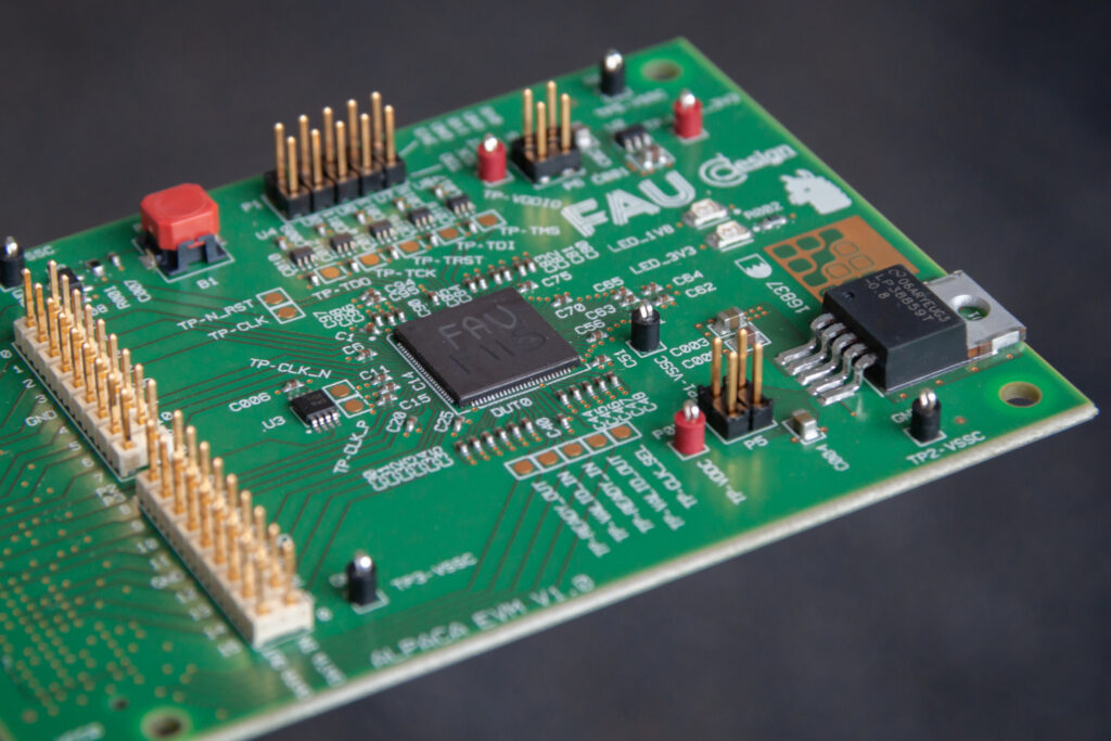 Das sogenannte Test-Board zeigt ein Board zum Testen des Chips, der sich verpackt im schwarzen Gehäuse in der Bildmitte befindet.