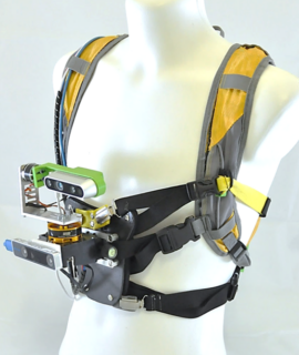 Das Assistenzsystem kann wie ein Rucksack am Körper angebracht werden. An der Körpervorderseite befindet sich eine 3D-Kamera, die das Assistenzsystem in Echtzeit mit Daten über die Beschaffenheit des Weges füttert. Bild: FAU