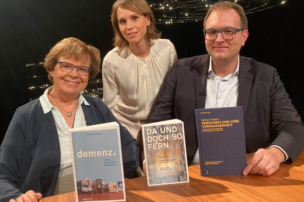 Irene Bopp und Michael Jungert sitzen nebeneinander an einem Tisch und schauen in die Kamera