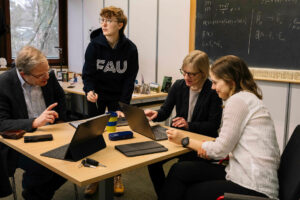 Wissenschaftlerinnen und Wissenschaftler sitzen gemeinsam an einem Tisch und mehreren Laptops.