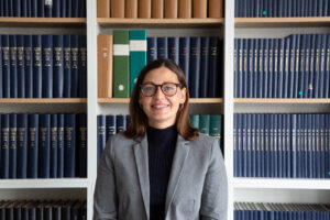 Frau mit Brille vor Bücherregal.