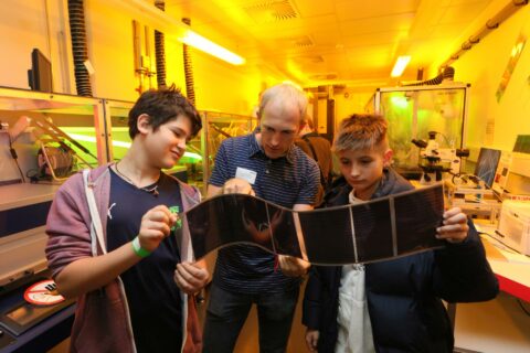 Ein Wissenschaftler zeigt zwei Jugendlichen etwas in einem Labor.