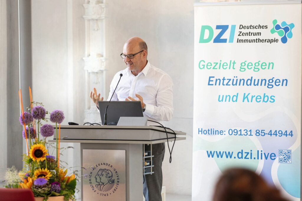 Georg Schett hält einen Vortrag, im Hintergrund: Banner des Deutschen Zentrums für Immuntherapie