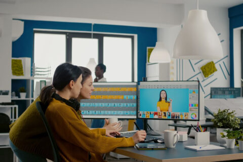 Two photographers advising for retouching client photo in creative media agency office. Graphic designers working at client assets on PC with two displays in photo editing software holding stylus pen