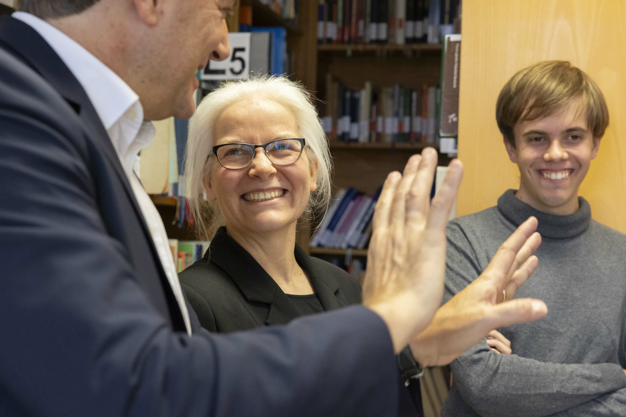 Eine Frau steht schaut lächelnd in die Kamera. Links und rechts neben ihr stehen zwei Männer. 