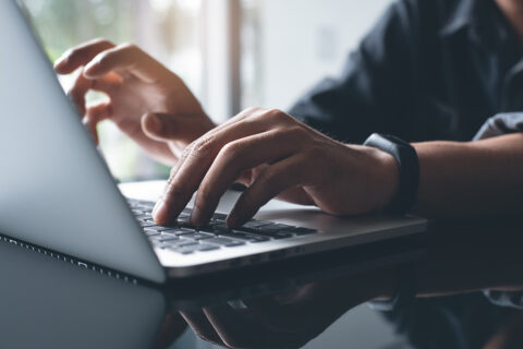 Mann tippt auf der Tastatur eines Laptops