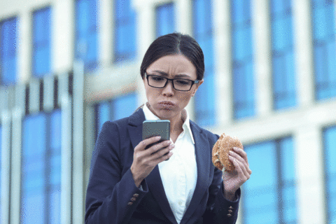 Frau isst Burger und schaut dabei auf Handy