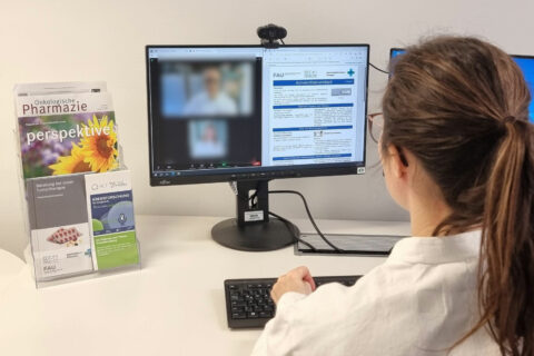 Forscherin in Kittel vor Monitor an Schreibtisch