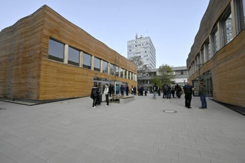 Zwei Gebäude aus Holz dazwischen Menschen auf kleinem Platz