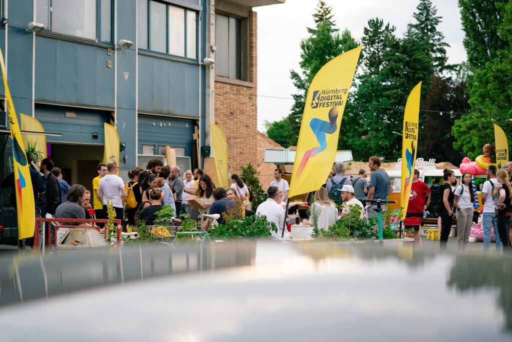 FAU-Vorträge und Workshops beim Nürnberg Digital Festival 2024. Hier Ein Foto der Closing Night mit menschen und gelben Fahnen zusammen auf Platz.