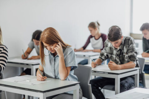 Menschen machen Prüfungen und sind über Tische gebeugt