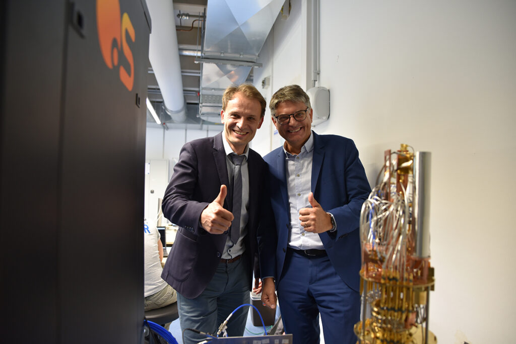 Eichler and Hornegger standing in front of a quantum computer showing a thumbs up gesture 