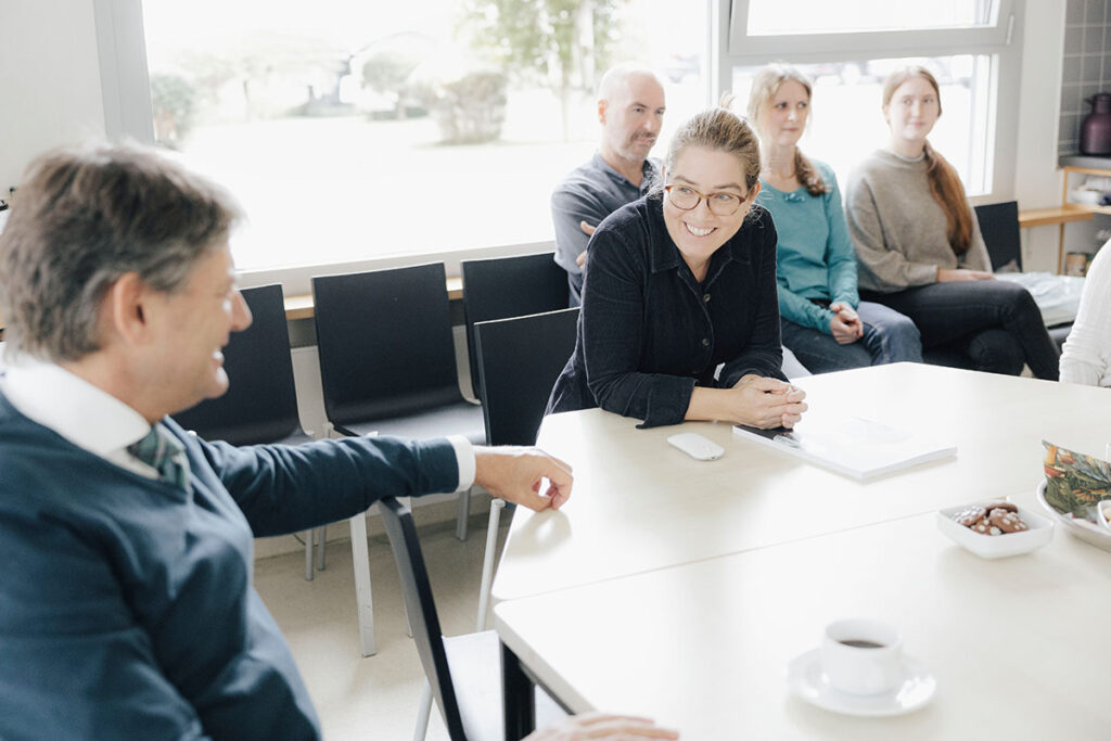 FAU President Joachim Hornegger visits Prof. Dr. Caroline Voskens, Professorship for Translational Immunodermatology, in her lab. They are seated at a table and chatting. Voskens is smiling. 