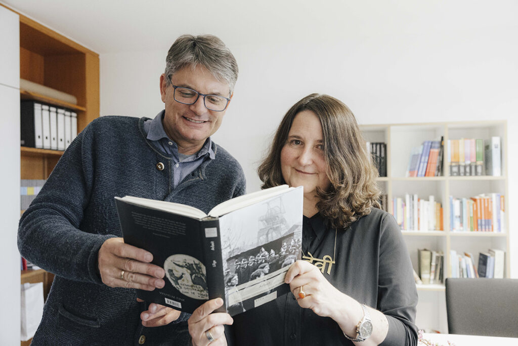 Prof. Lillge und FAU-Präsident Hornegger mit einem Buch, Prof. Lillge schaut über den Rand hinweg in die Kamera. 