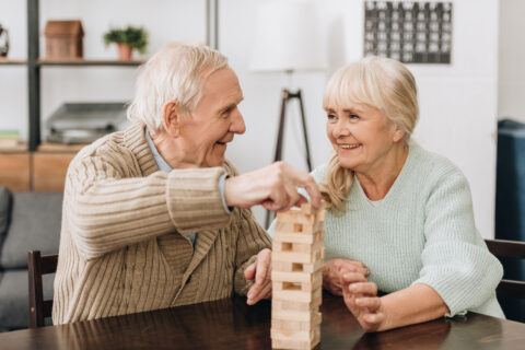 Lächelnde Rentner spielen Jenga auf einem Tisch