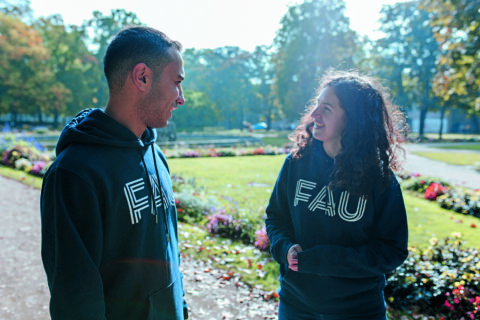 Zwei junge Menschen in FAU-Pullis unterhalten sich freundlich im Schlossgarten, Erlangen
