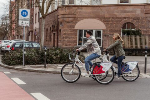 Ein Mann und eine Frau fahren auf Fahrrädern durch die Erlanger Innenstadt, die Fahrräder sind mit "VAG Rad" beschriftet
