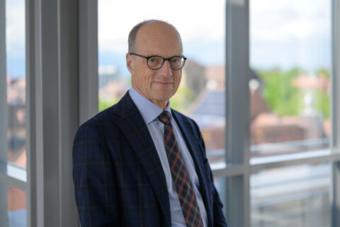 Herr Iro, ein Mann mittleren Alters mit Brille und Anzug, lächelt in die Kamera.