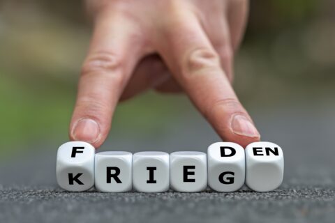 Finger stoßen Würfel um machen aus dem Wort Krieg das Wort Frieden.