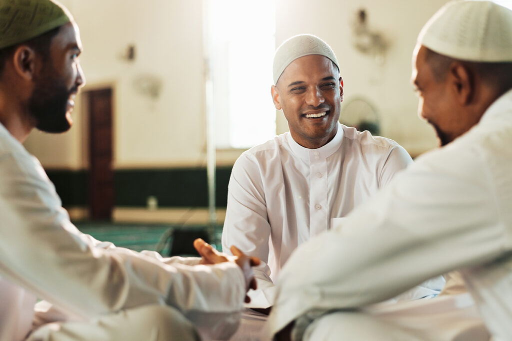 3 muslimische Männer unterhalten sich lächelnd in einer Moschee.