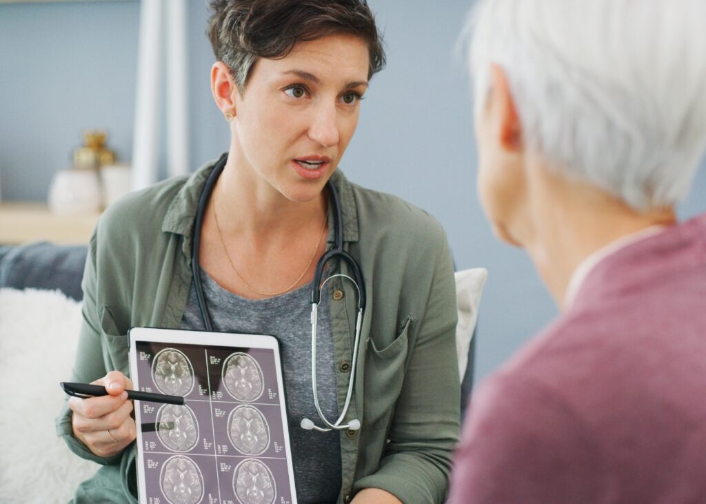 Ärztin mit dunklen kurzen Haaren zeigt Seniorin auf Tablet Gehirnscann und erklärt.