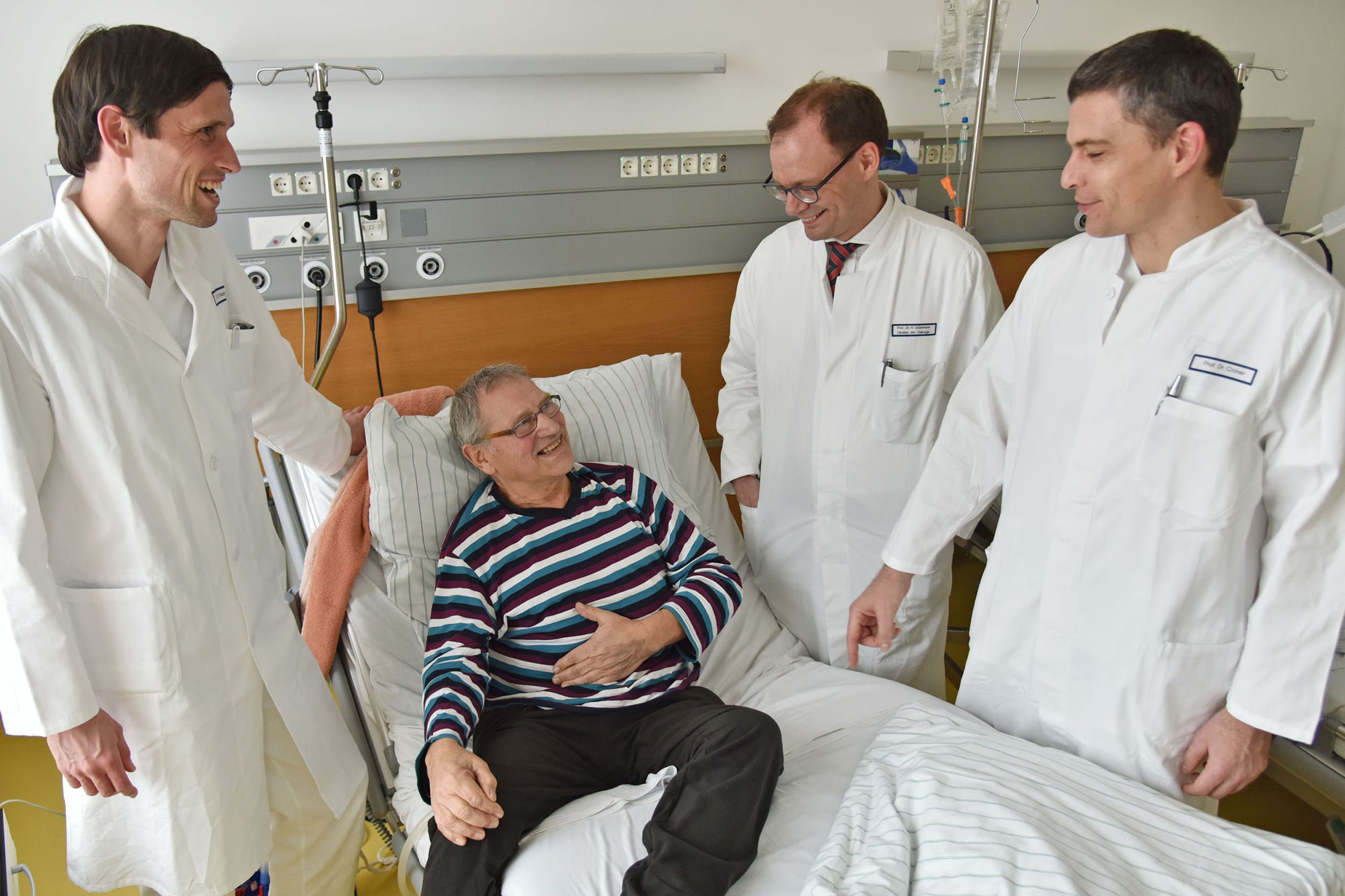 Er kann schon wieder lachen: Patient Rolf Arnold mit den behandelnden Ärzten (von links) Dr. Christian Krautz, Prof. Dr. Robert Grützmann und Prof. Dr. Roland Croner. (Bild: Uni-Klinikum Erlangen)