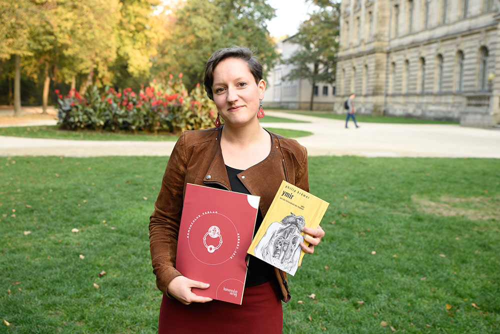 Mitarbeiterin im Schlossgarten mit zwei Büchern in der Hand
