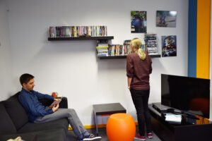 Blick auf die Sofaecke: Ein Student sitzt auf der Couch und liest; eine andere Studentin schaut sich die Videos an