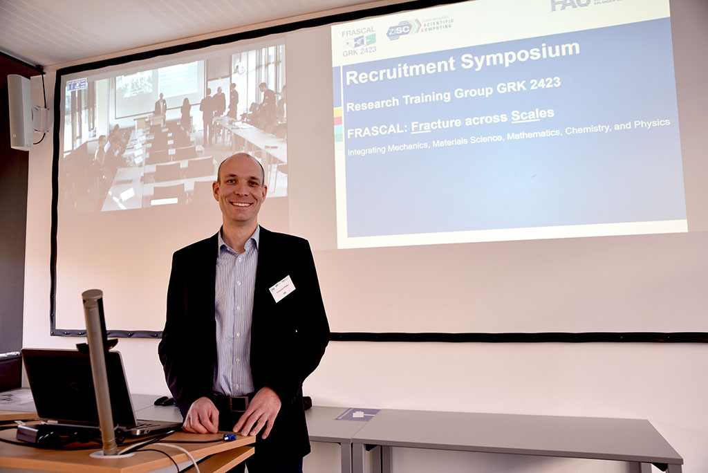 Einzelbild von Sebastian Pfaller und im Hintergrund eine Live-Übertragung und eine FAU-Präsentationsfolie