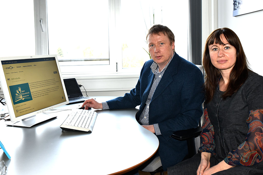 Fred Neumann (links) und Elena Coroian (rechts) sitzen vor einem Computer und blicken in dier Kamera.