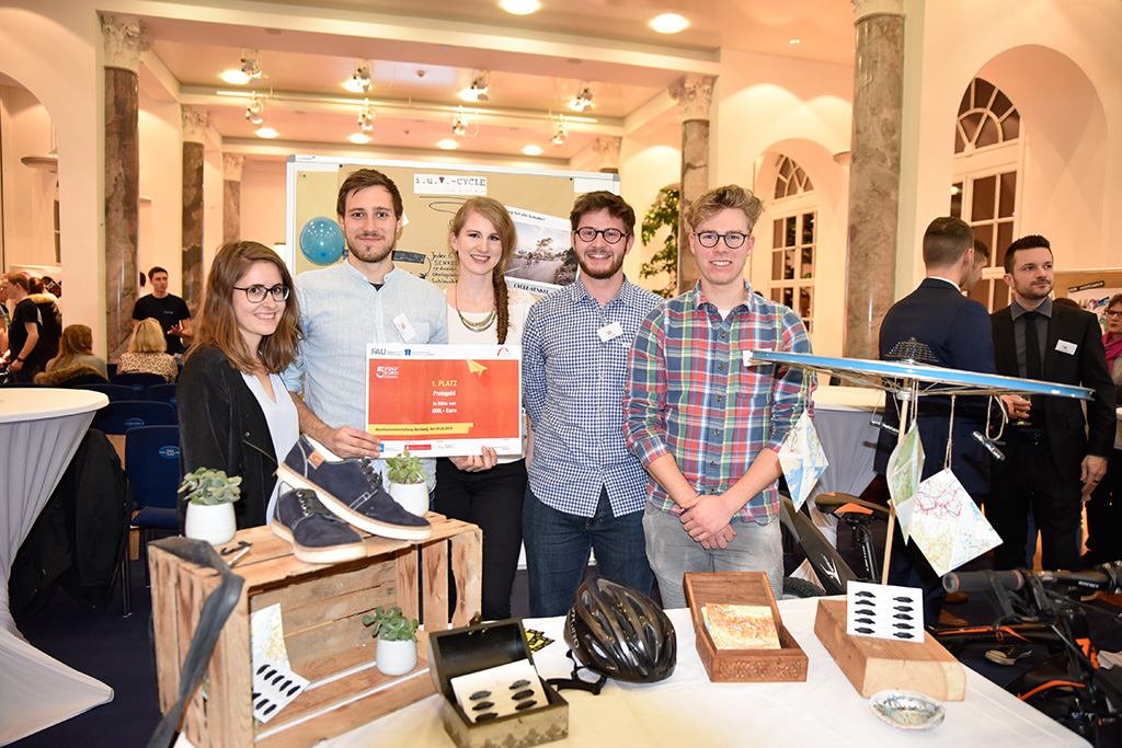 Gruppenbild der fünf Studierenden. Im Vodergrund ist ein Tisch mit einer Fahrradfelge, Schnürsenkeln aus Fahrradschläuchen und Turnschuhen abgebildet.
