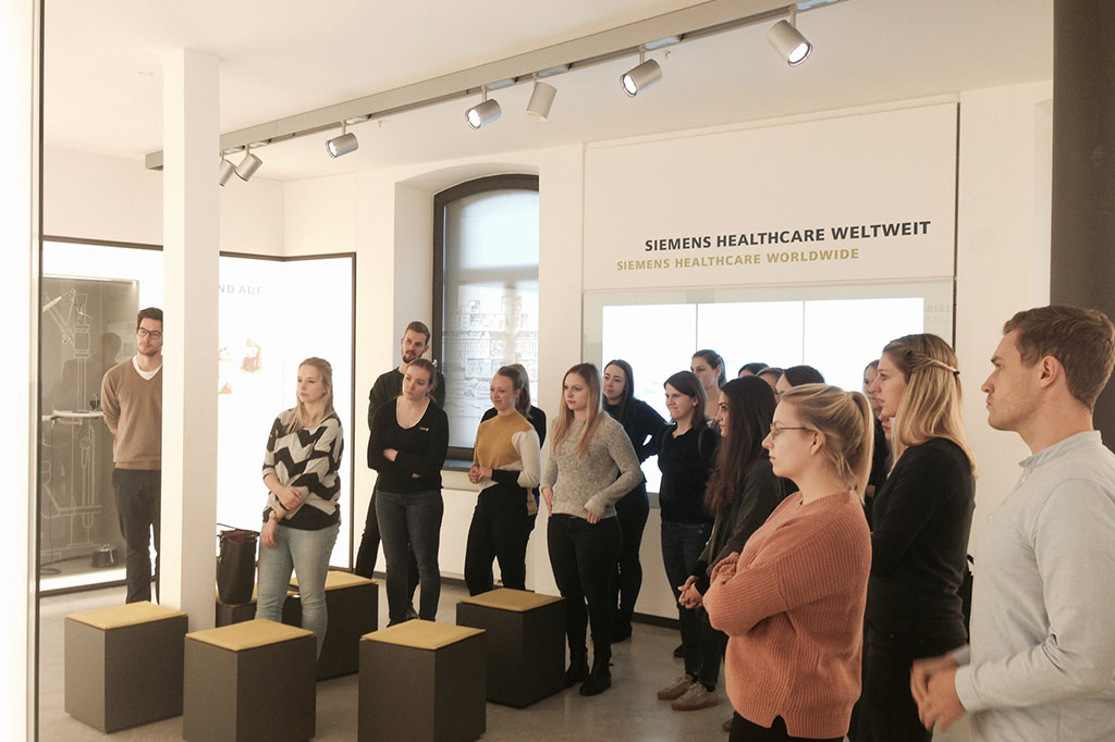 Eine Gruppe von menschen, die sich im SiemensMed Museum gerade etwas anschaut.