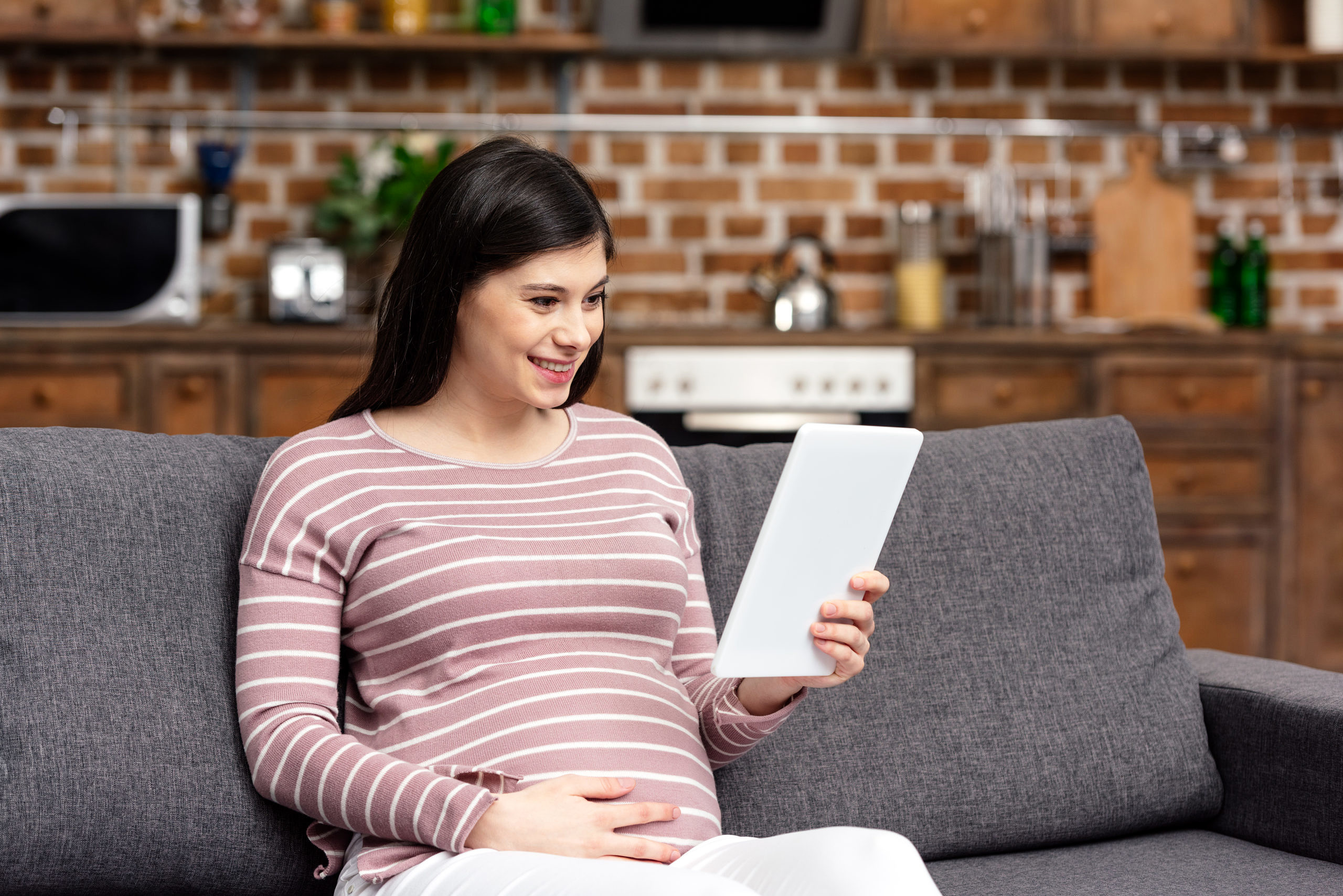 Smiling young pregnant woman using digital tablet at home