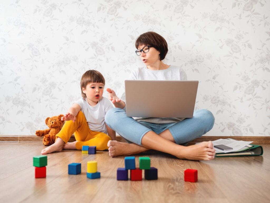Eine Mutter sitzt mit Laptop im Spielzimmer ihres Sohnes.