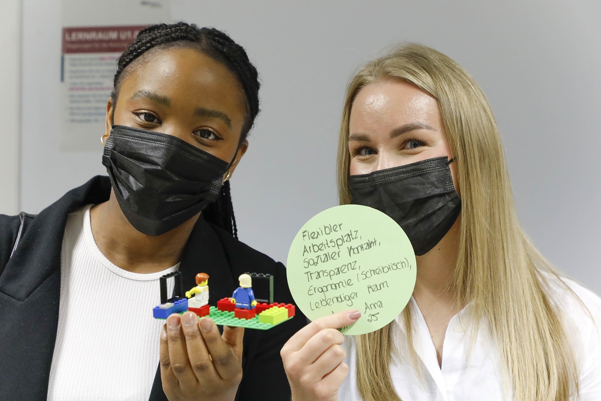 Frau mit Lego-Modell und Frau mit beschriebener Karte