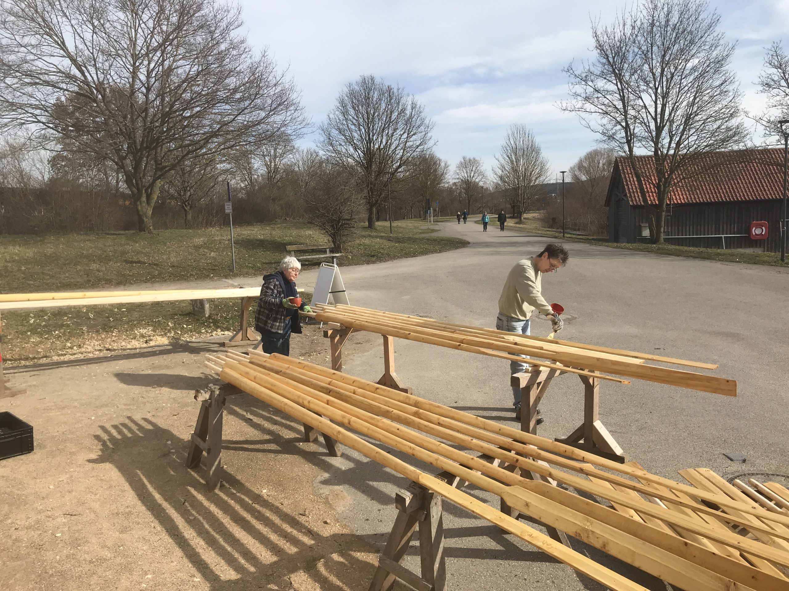 Zwei Menschen bringen Schutzlack auf Holzriemen auf