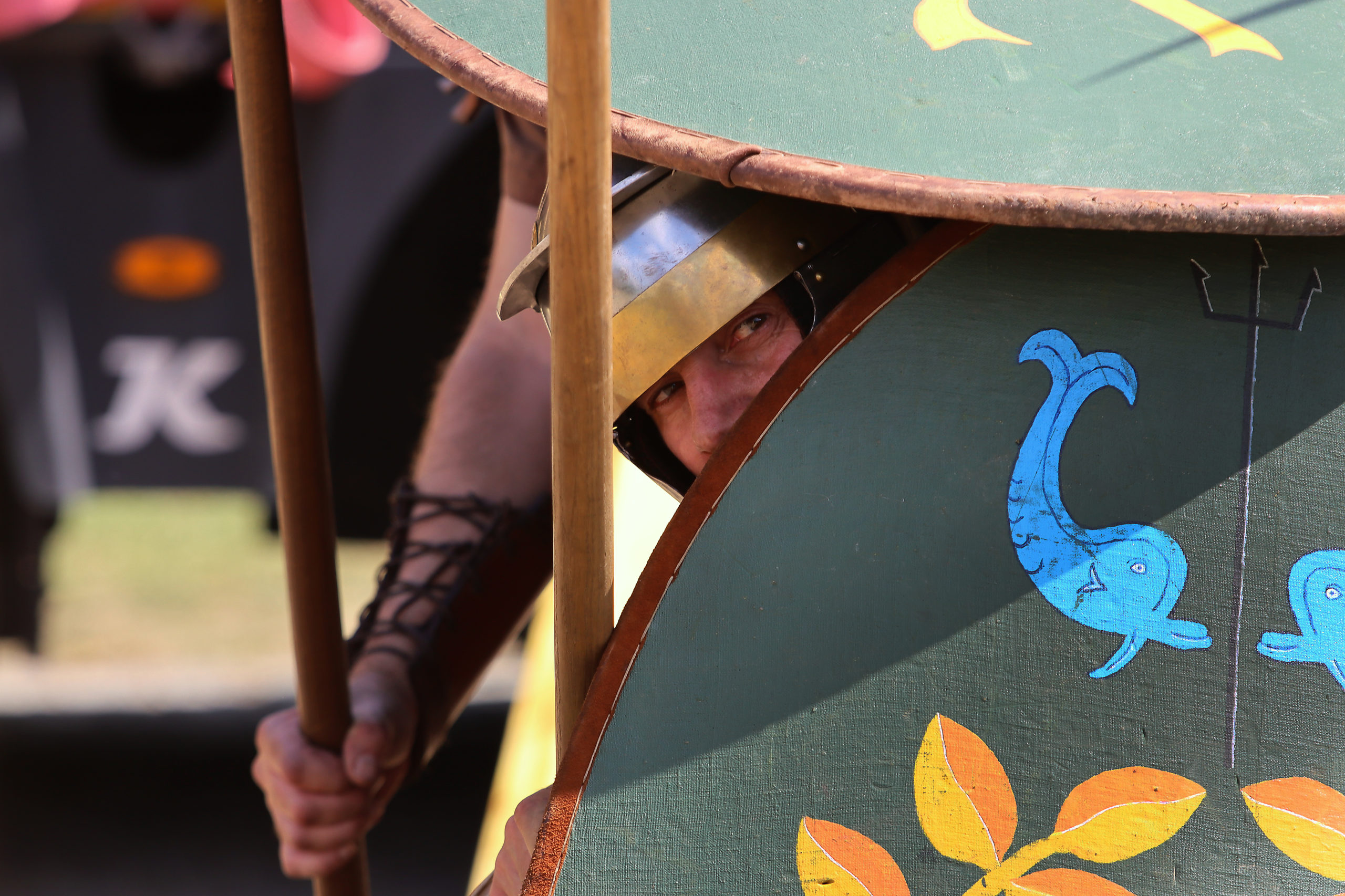 Hinter einem Schild schaut ein als römischer Soldat hervor. Nur seine Augen, seine Nase und sein Speer schauen hervor.