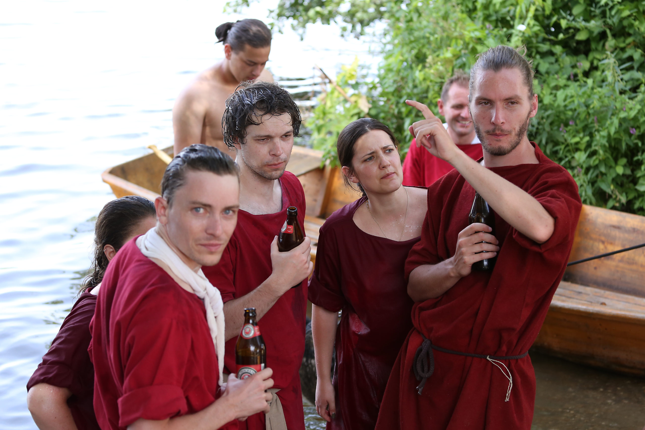 Ruderinnen und Ruderer eines Römerbootes stehen am Ufer und trinken gemeinsam Bier.