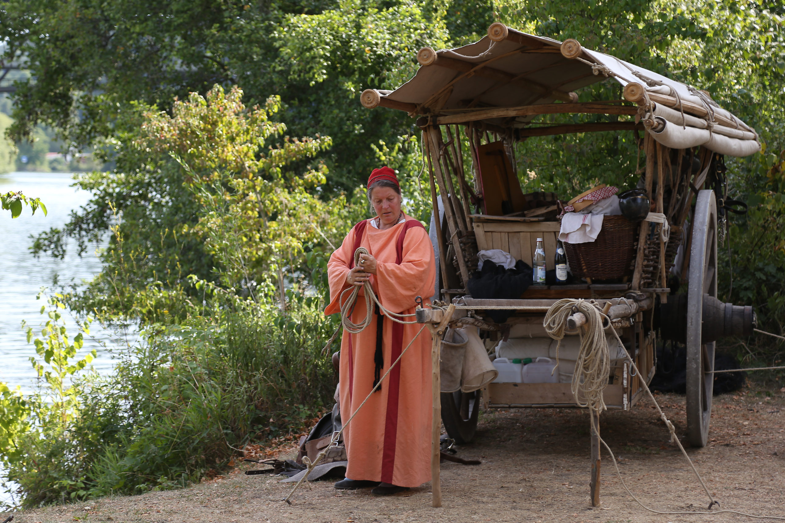 Am DOnauufer steht ein römischer Wagen und eine Reenactment-Darstellerin in orange-rotem Gewand.