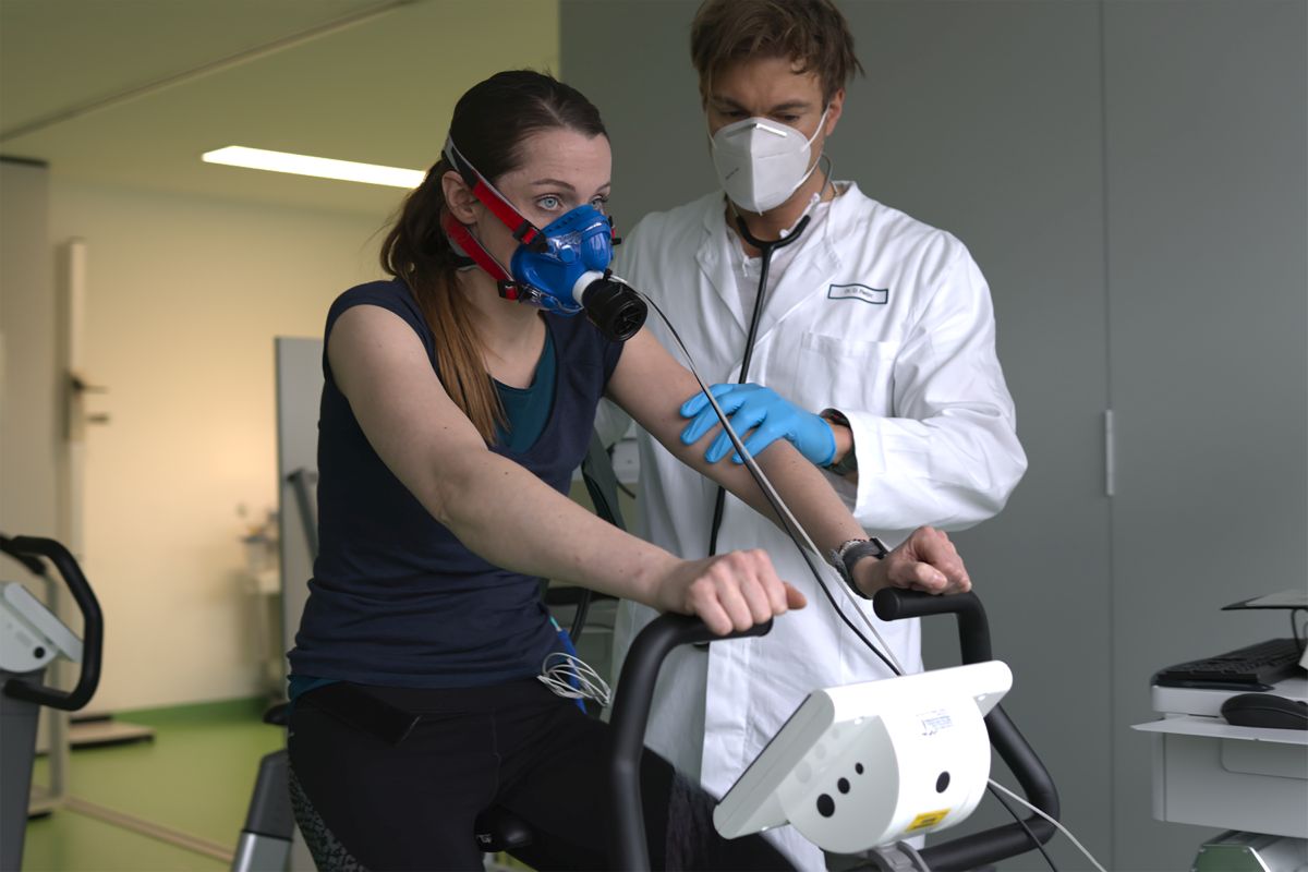 Patientin bei der Spiroergometrie, neben ihr Sportmediziner in Kittel, ermitteln die Leistungsfähigkeit des LOW-HIIT