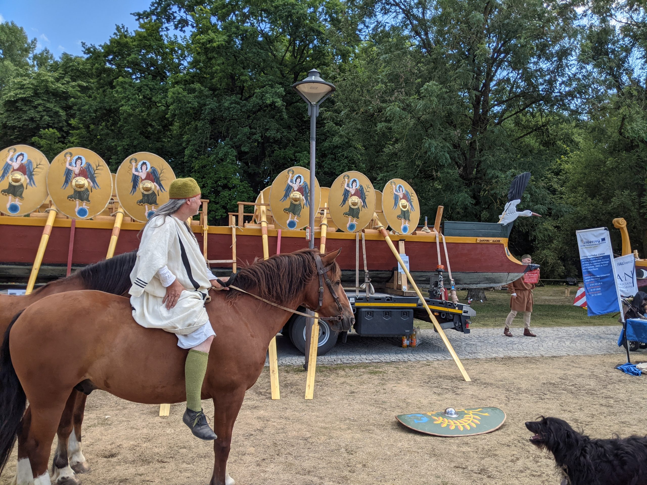 Ein Reenactment-Darsteller sitzt auf einem Pferd und sieht zu, wie ein Römerboot auf einem LKW angeliefert wird.