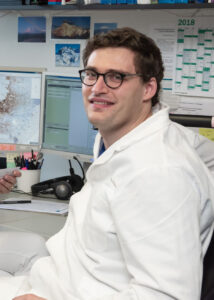 Ein Mann mit weißem Arztkittel sitzt an einem Schreibtisch.